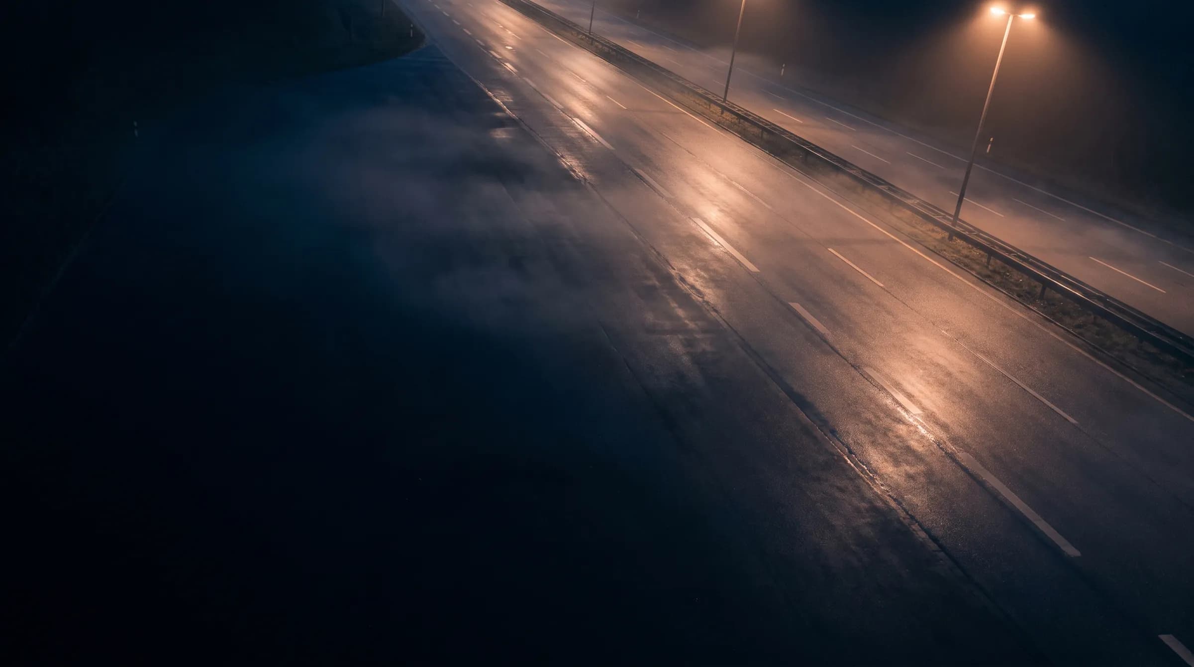 Nächtliche Ausfallstraße bei Regen, nasse Fahrbahn im Laternenlicht